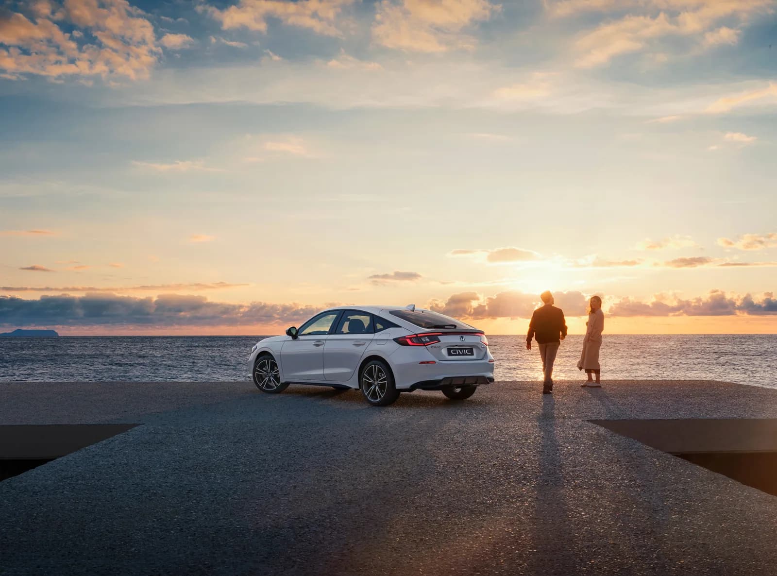 Honda Civic — vedere din spate, la apus, cu două persoane lângă mașină