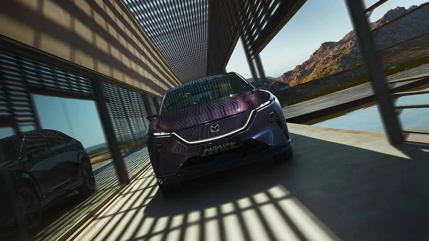 Mazda CX-6e violetă, văzută din față, sub un pasaj cu umbre