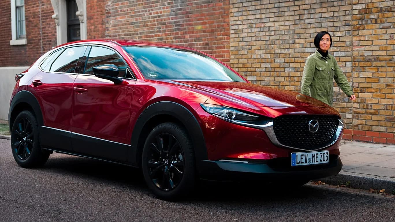 Mazda CX-30 roșie oprită pe o stradă, cu un pieton trecând pe trotuar