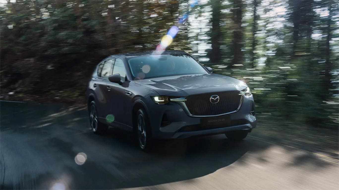 Mazda CX-60 gri, în mers pe un drum printre copaci
