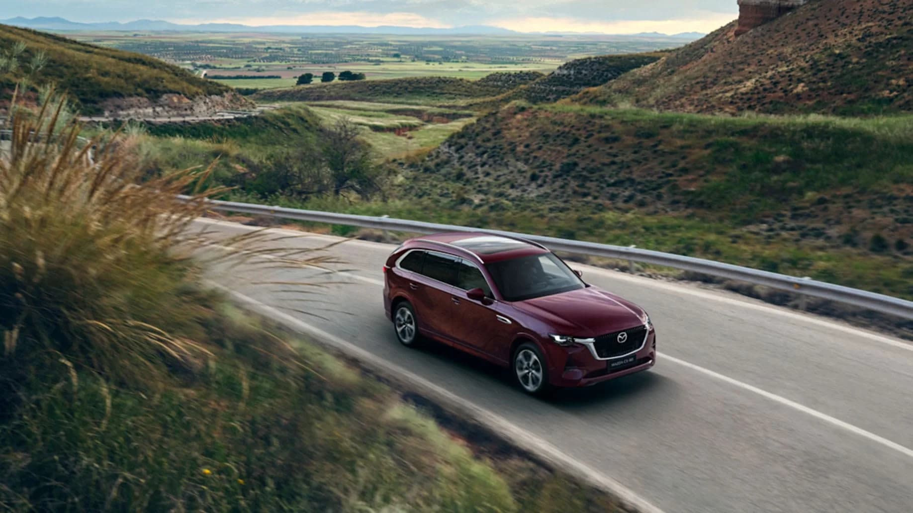 Mazda CX-80 roșu-închis în mers pe un drum de munte