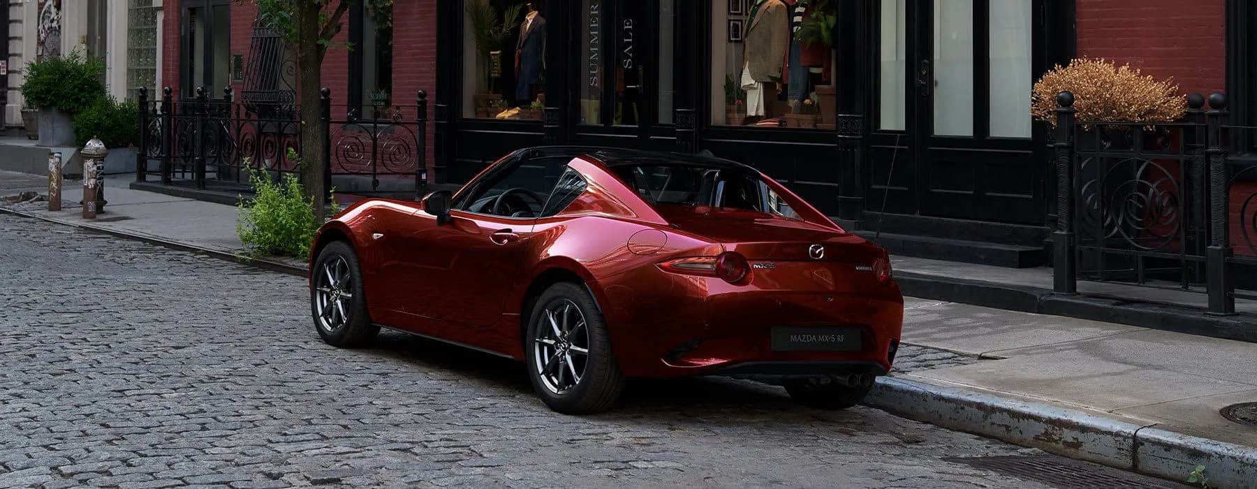 Mazda MX-5 RF roșie, cu plafon rigid, parcată pe o stradă pavată
