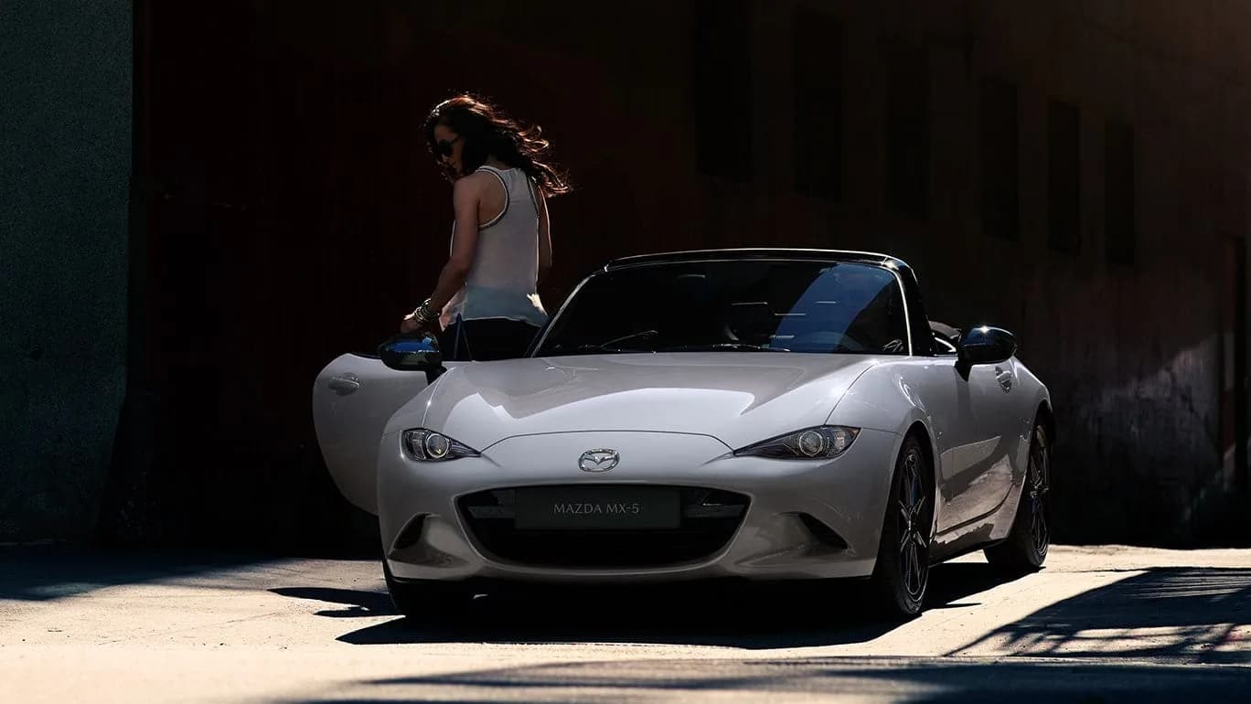 Mazda MX-5 — MX-5 albă cu plafonul textil închis, pe o stradă îngustă