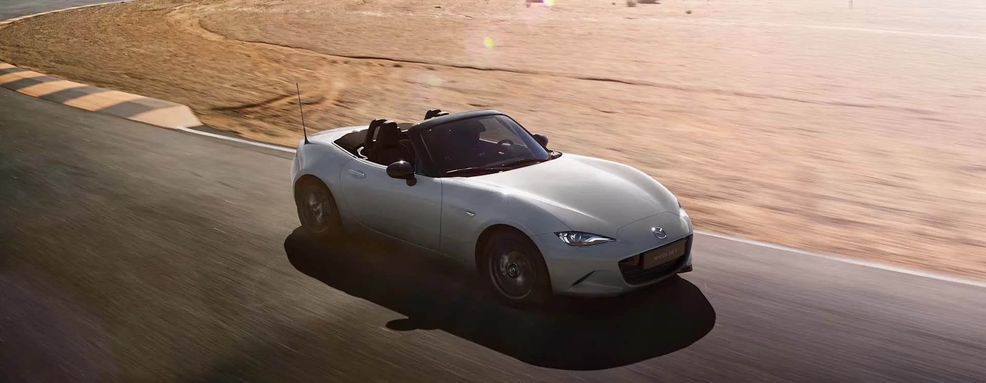 Mazda MX-5 albă cu plafonul deschis, în mers pe un drum de deșert